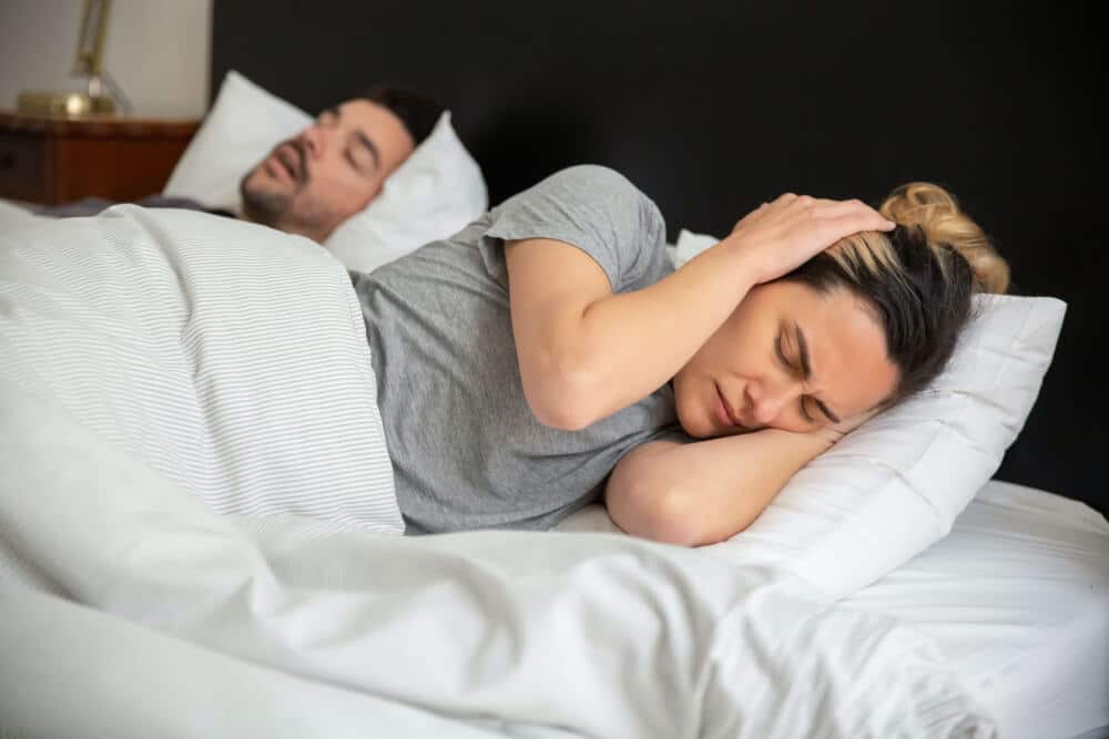 Woman covering ears because of man snoring